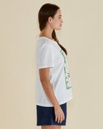 Woman wearing a white t-shirt with a pineapple graphic and 'Paradise' text on a beige background Ellia Crew Tee White