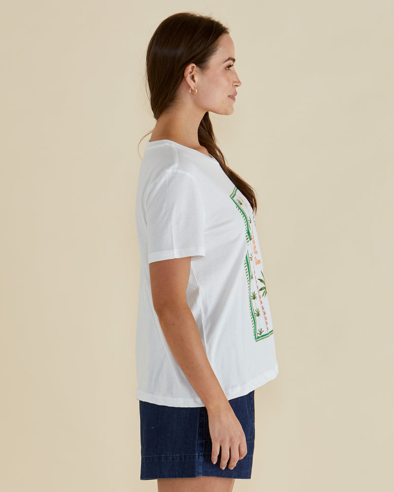Woman wearing a white t-shirt with a pineapple graphic and 'Paradise' text on a beige background Ellia Crew Tee White