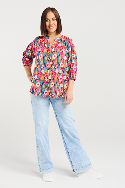 Woman wearing a colorful floral blouse and light blue jeans on a white background Evie Shirt Canvas Bloom