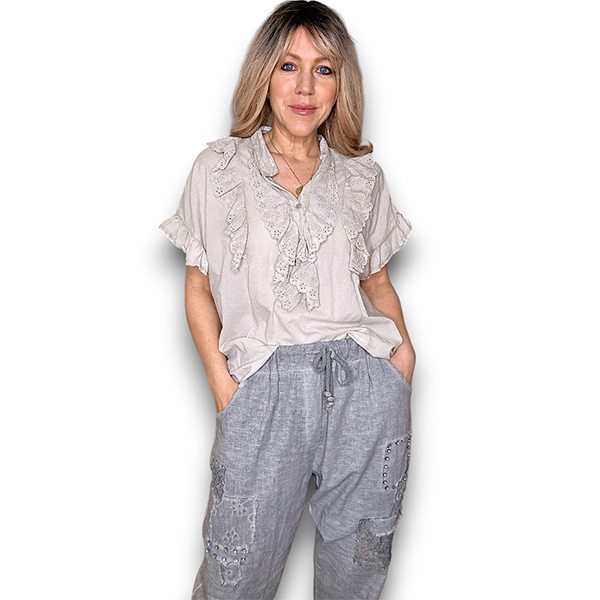 Woman wearing a light-colored blouse with lace details and gray pants on a white background
Eyelet Top Pale Beige