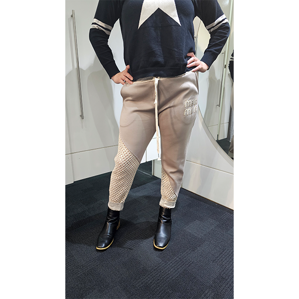Person wearing a navy sweater with white star design and beige pants with mesh panels in a bathroom.