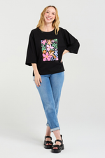 Woman wearing a black top with a colorful floral design and blue jeans on a white background
Kate T-Shirt Black