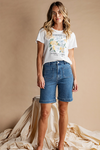 Woman wearing a white t-shirt with a graphic design and blue denim shorts against a beige background
Limoncello Tee Vintage White
