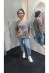 Woman standing in a fitting room wearing a Taupe t-shirt with floral design and blue jeans.