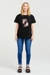 Woman wearing a black t-shirt with a graphic design and blue jeans on a white background
Livia T-Shirt Black