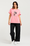 Woman wearing a pink t-shirt with a graphic design and black pants on a white background
Livia T-Shirt Pink