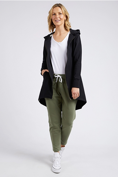 Woman wearing a black coat, white shirt, green pants, and white sneakers on a white background
Mara Zip Hoodie Black