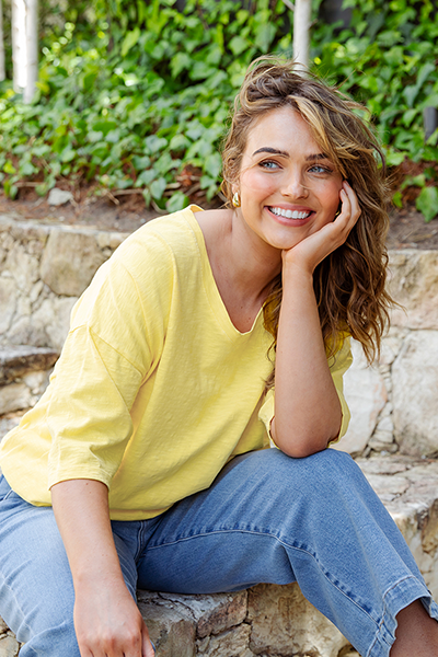 Woman in a yellow shirt and blue jeans sitting on stone steps with greenery in the background
Mazie Vee Neck Top Lemon