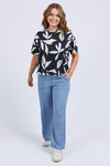 Woman wearing a black and white patterned top with blue pants on a white background
Mimosa Tee Black