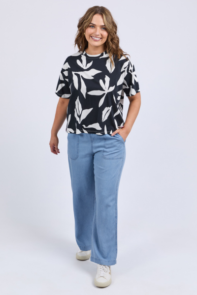 Woman wearing a black and white patterned top with blue pants on a white background
Mimosa Tee Black
