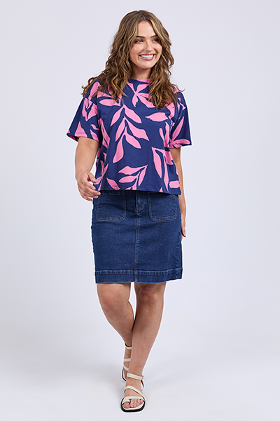 Woman wearing a blue and pink leaf-patterned top with a denim skirt on a white background
Mimosa Tee Blue Depths