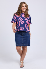 Woman wearing a blue and pink leaf-patterned top with a denim skirt on a white background
Mimosa Tee Blue Depths