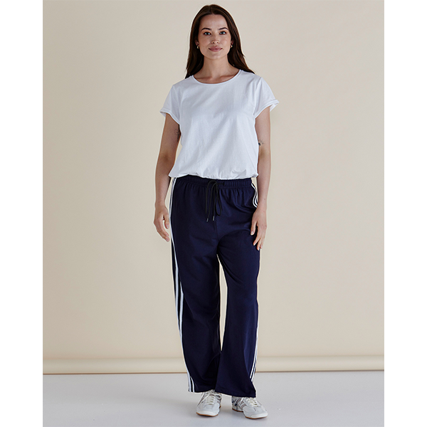 Woman wearing a white t-shirt and navy pants with white stripes on a beige background