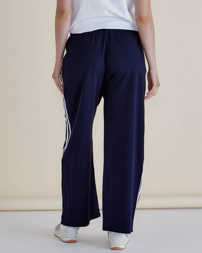 Navy blue pants with white stripes worn by a person on a beige background