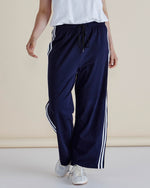Navy track pants with white stripes worn by a person on a beige background