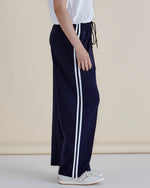 Navy track pants with white stripes worn by a person on a beige background