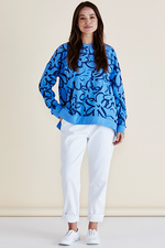 Woman wearing a blue patterned sweater and white pants against a beige background
Palma Sweat Blue Floral