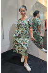 Woman wearing a floral dress standing in front of a mirror. Pleat Front Dress Green