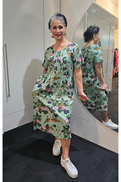 Woman wearing a floral dress standing in front of a mirror. Pleat Front Dress Green