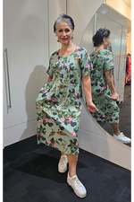 Woman wearing a floral dress standing in front of a mirror. Pleat Front Dress Green