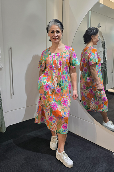 Woman wearing a colorful floral dress standing in front of a mirror. Pleat Front Dress Orange