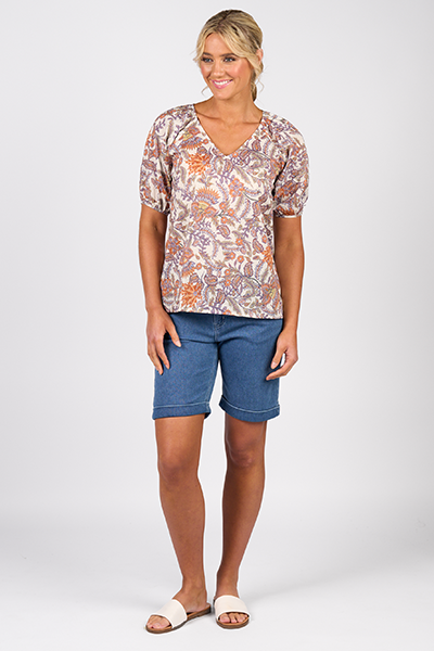 Woman wearing a patterned top and blue shorts on a white background