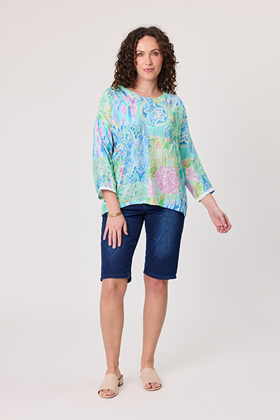 Woman wearing a colorful floral blouse and blue shorts on a white background Rimini Top Aqua