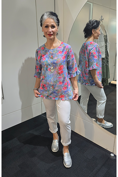 Woman wearing a floral blouse and white pants standing in front of a mirror. Round Neck Top Blue