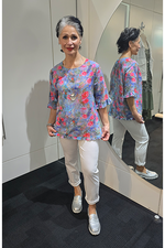 Woman wearing a floral blouse and white pants standing in front of a mirror. Round Neck Top Blue