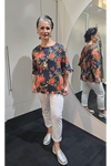 Woman wearing a floral blouse and white pants standing in front of a mirror. Round-Neck-Top-Multi