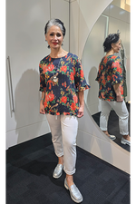 Woman wearing a floral blouse and white pants standing in front of a mirror. Round-Neck-Top-Multi