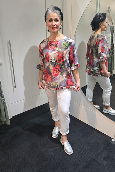 Woman wearing a floral top and white pants standing in front of a mirror. Round Neck Top Taupe