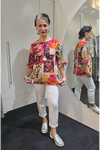 Woman wearing a colorful floral blouse and white pants standing in front of a mirror. Round_Neck_Top_Pink