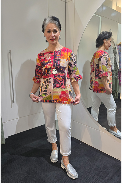 Woman wearing a colorful floral blouse and white pants standing in front of a mirror. Round_Neck_Top_Pink