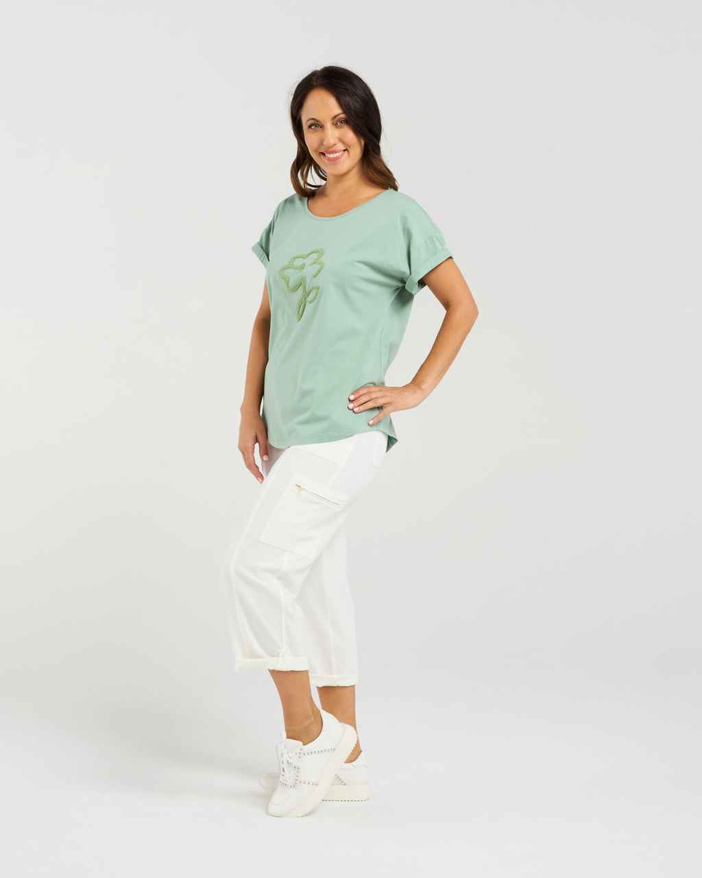 Woman wearing a light green t-shirt with a graphic design on a white background Lily Top Sage