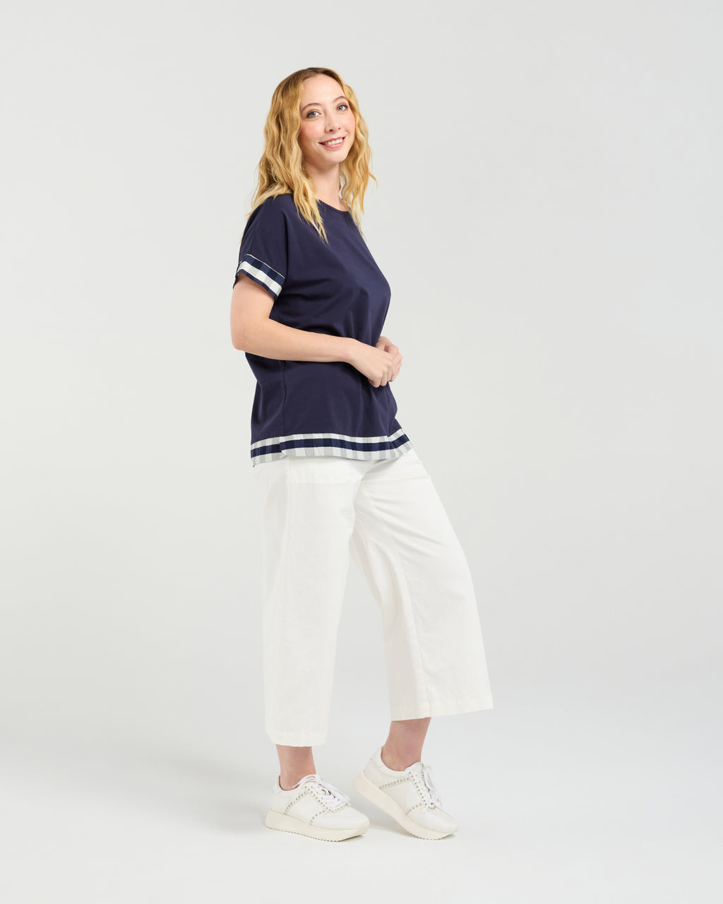 Woman wearing a navy blue top with white trim and white pants on a white background Luna Top Ink Check