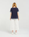 Woman wearing a navy blue top with white trim and white pants on a light gray background Luna Top Ink Check