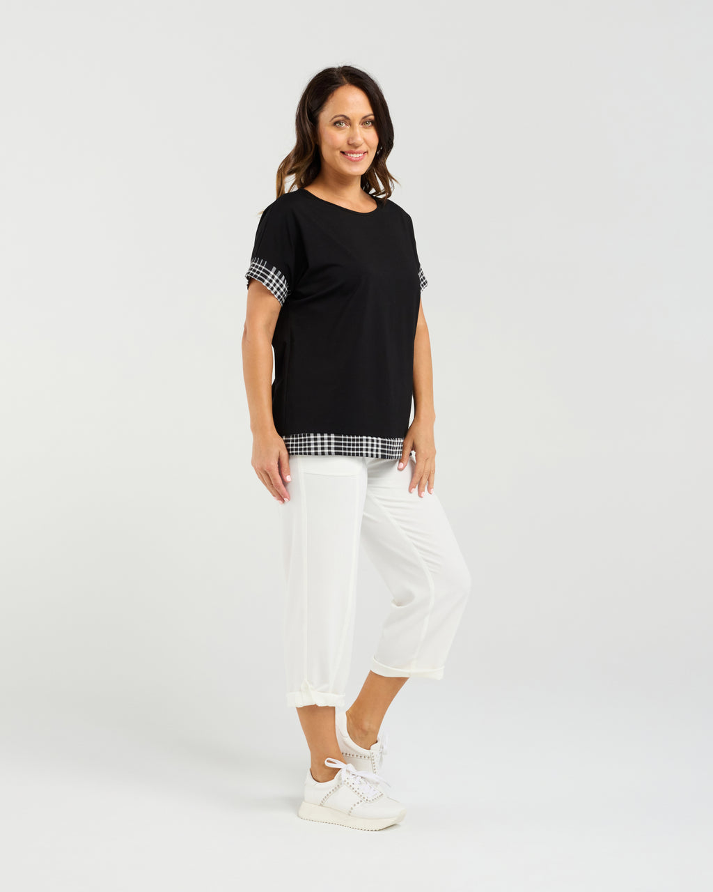 Woman wearing a black top with checkered sleeves and white pants on a white background Luna Top Black Check
