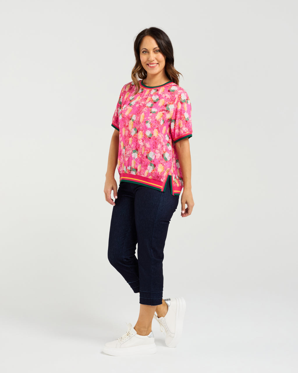 Woman wearing a pink floral top and navy pants on a white background Zoe Top Petal Confetti