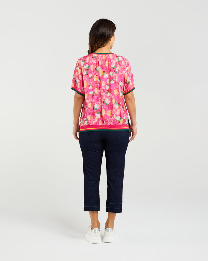 Woman wearing a pink floral top and navy pants on a white background Zoe Top Petal Confetti