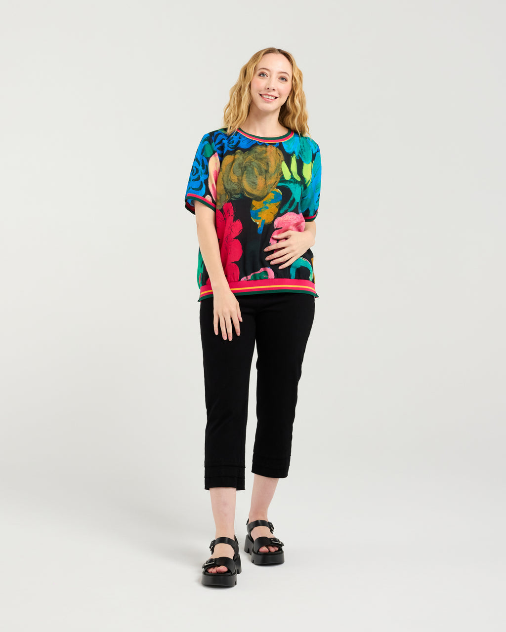 Woman wearing a colorful floral top and black pants on a white background Zoe Top Midnight Fern
