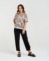 Woman wearing a patterned top and black pants on a white background Zoe Top Sage Mosaic