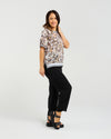 Woman wearing a floral blouse and black pants on a white background Zoe Top Sage Mosaic
