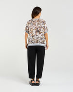 Woman wearing a patterned top and black pants on a white background Zoe Top Sage Mosaic