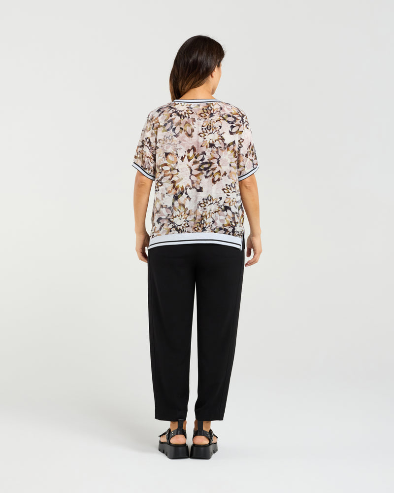Woman wearing a patterned top and black pants on a white background Zoe Top Sage Mosaic