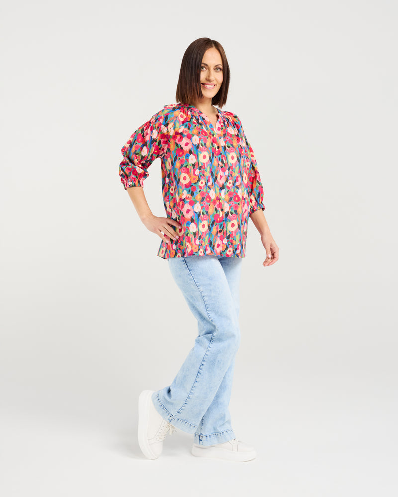 Woman wearing a colorful floral blouse and light blue jeans on a white background Evie Shirt Canvas Bloom