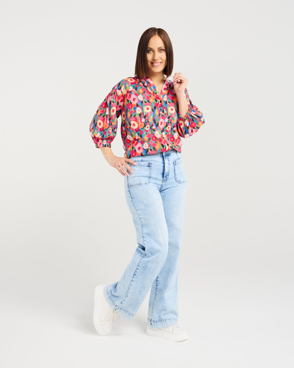 Woman wearing a colorful floral blouse and light blue jeans on a white background Evie Shirt Canvas Bloom