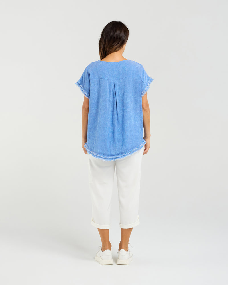 Person wearing a blue shirt and white pants on a plain background
Lilah Top Blue