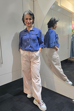 Woman wearing a blue denim shirt and beige pants standing in front of a mirror. Saffra Relax Leg Jean Pink