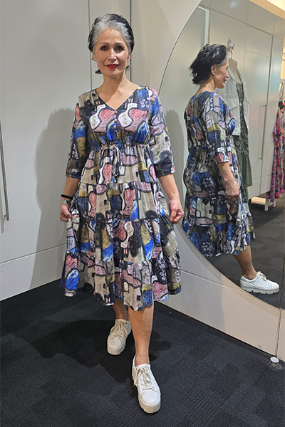 Woman wearing a patterned dress and white sneakers standing in front of a mirror. Tie Front Dress Multi